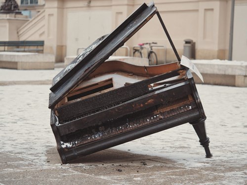 Ødelagt klaver ligger på en snebeklædt fliseplads